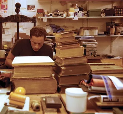 Luke Hornus at his bench among books awaiting repair